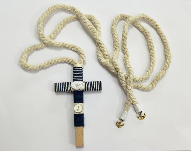 Cruz de comunión en madera con hilo azul marino y blanco a rayas, inicial personalizada y cordón trenzado con anclas doradas.
